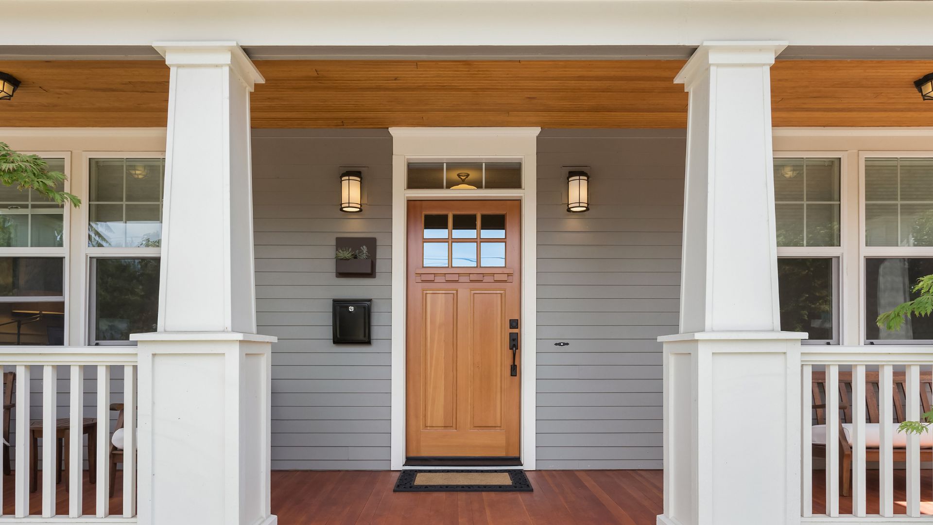 Wooden front door with white columns and gray siding on modern house