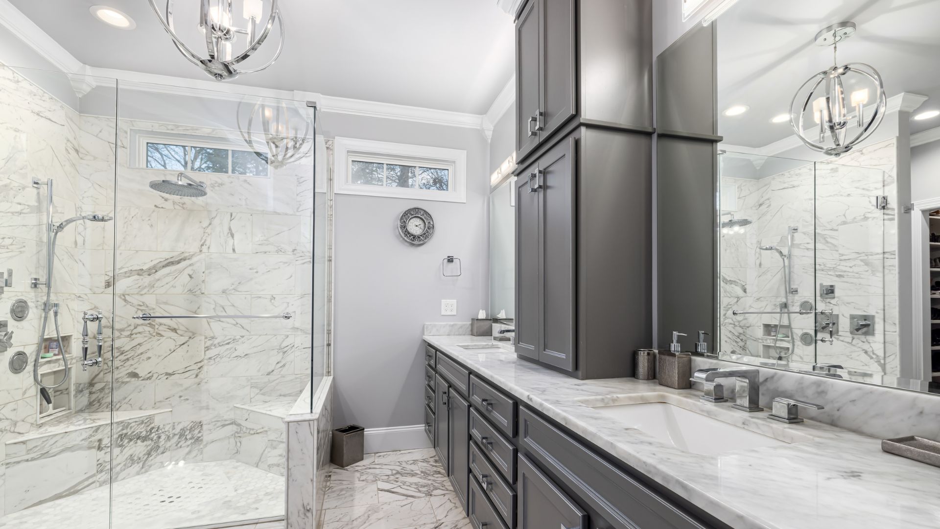 Modern bathroom with marble tiles, gray cabinets, and glass shower